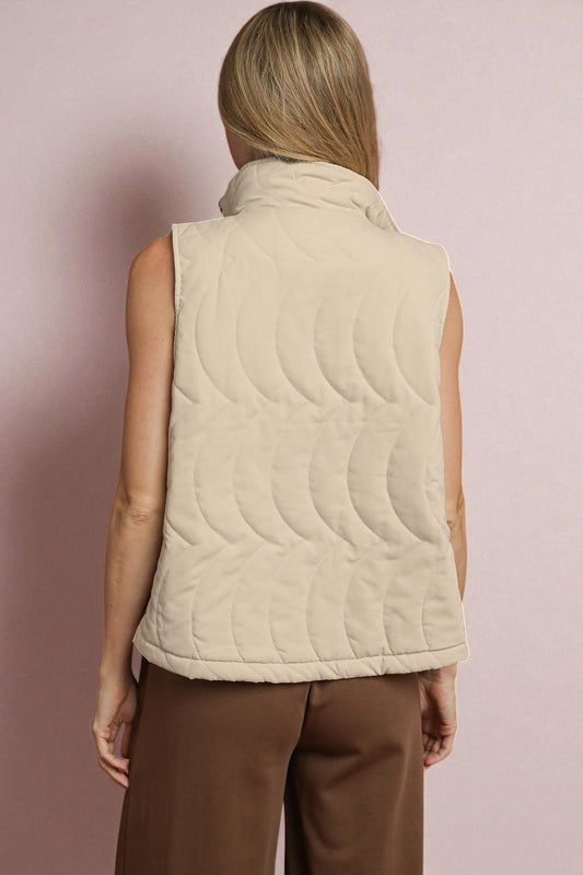 Person wearing a beige quilted vest against a pink background