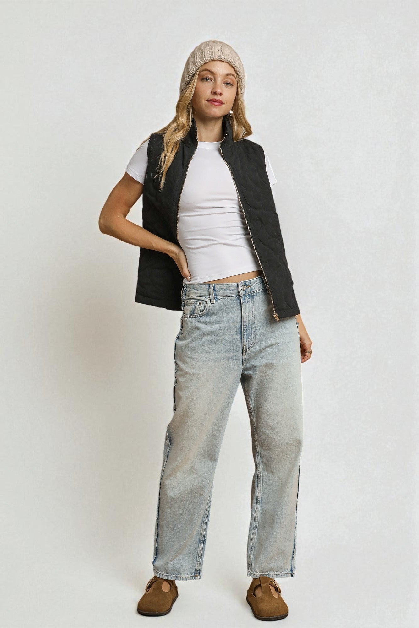 Person wearing a white t-shirt, black vest, light blue jeans, and brown shoes on a white background