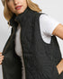 Person wearing a black quilted vest over a white shirt on a light gray background