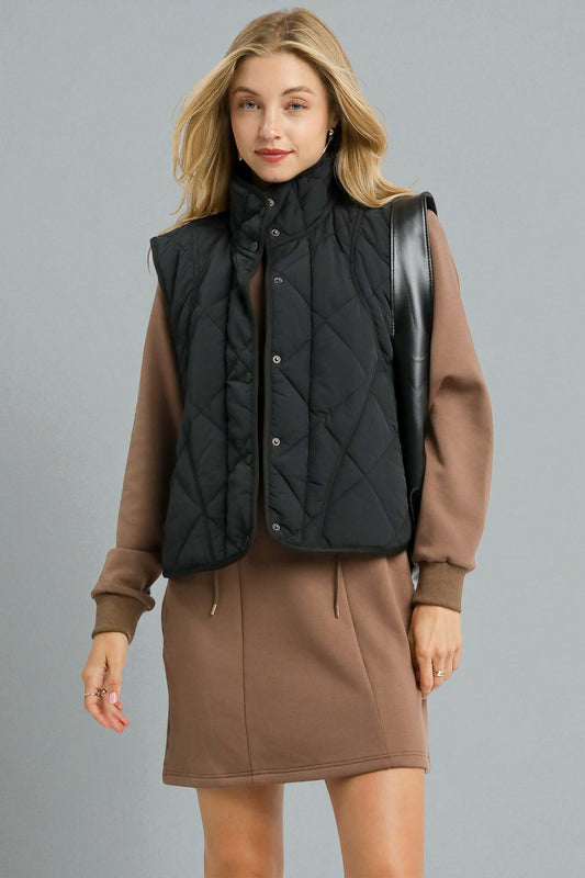 Woman wearing a black quilted vest over a brown outfit on a gray background