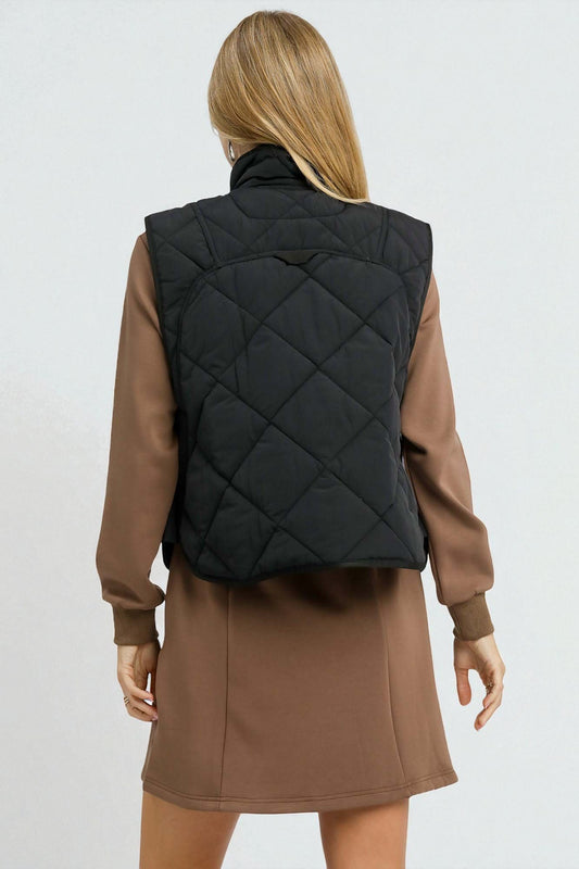 Person wearing a black quilted vest over a brown dress on a white background