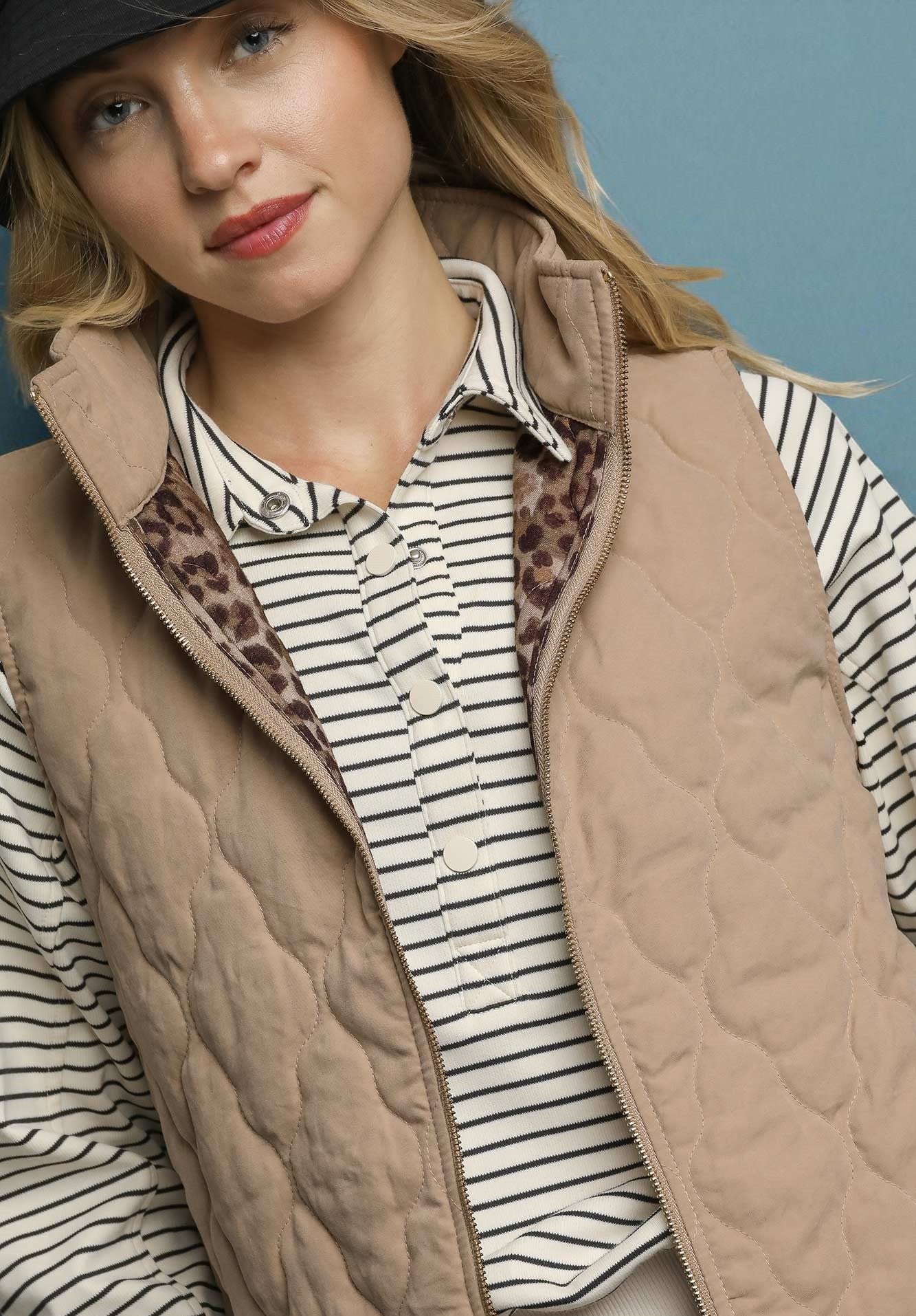 Woman wearing a beige quilted vest over a striped shirt with a blue background