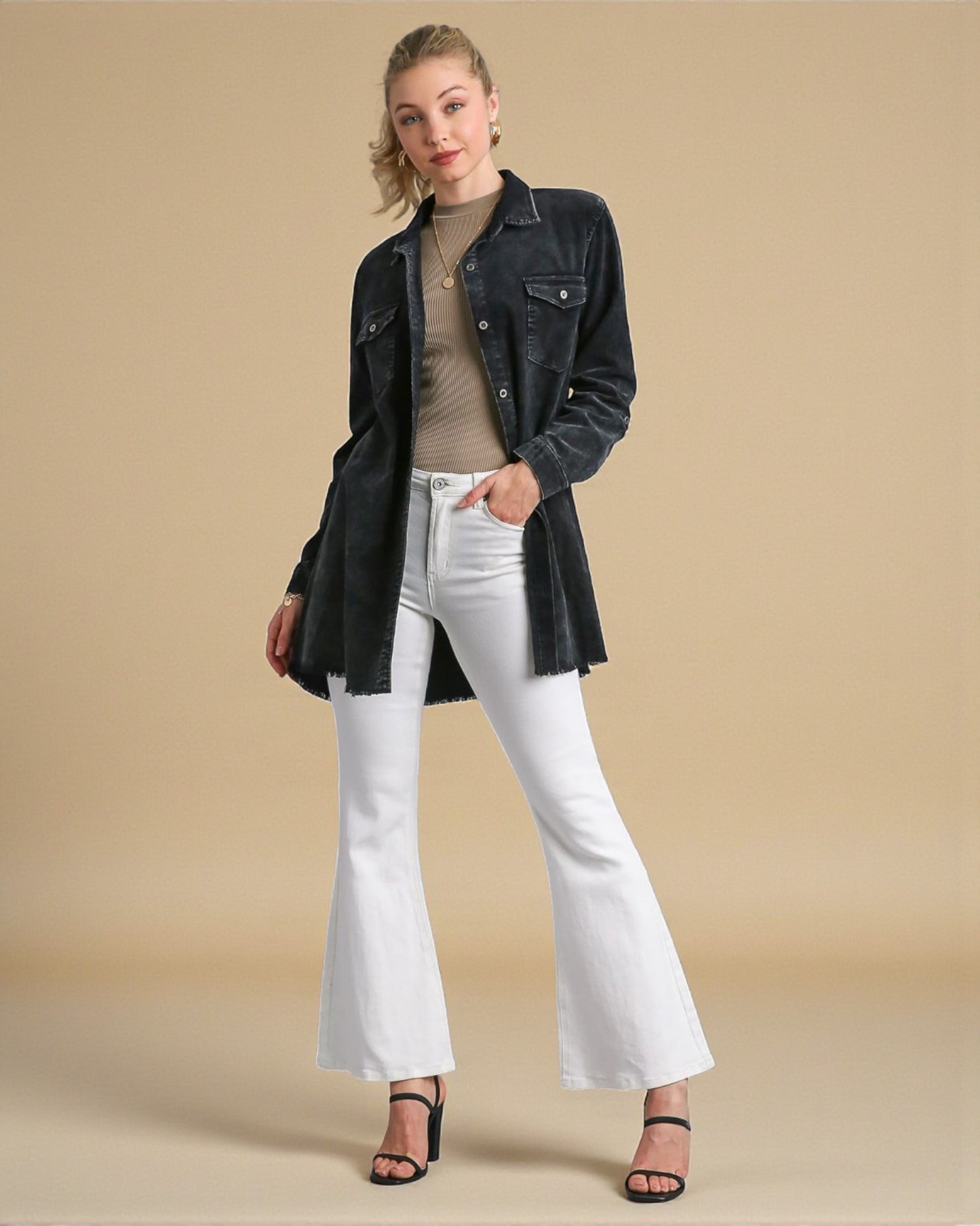 Woman wearing a black denim jacket, beige top, white jeans, and black sandals on a beige background