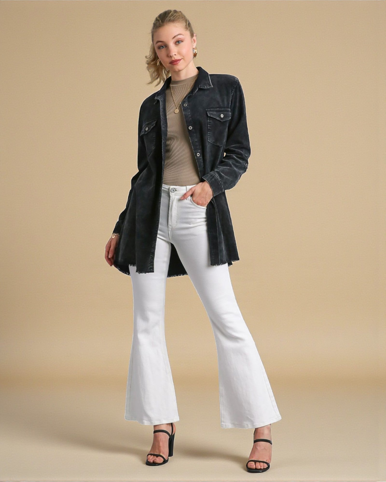 Woman wearing a black denim jacket, beige top, white jeans, and black sandals on a beige background