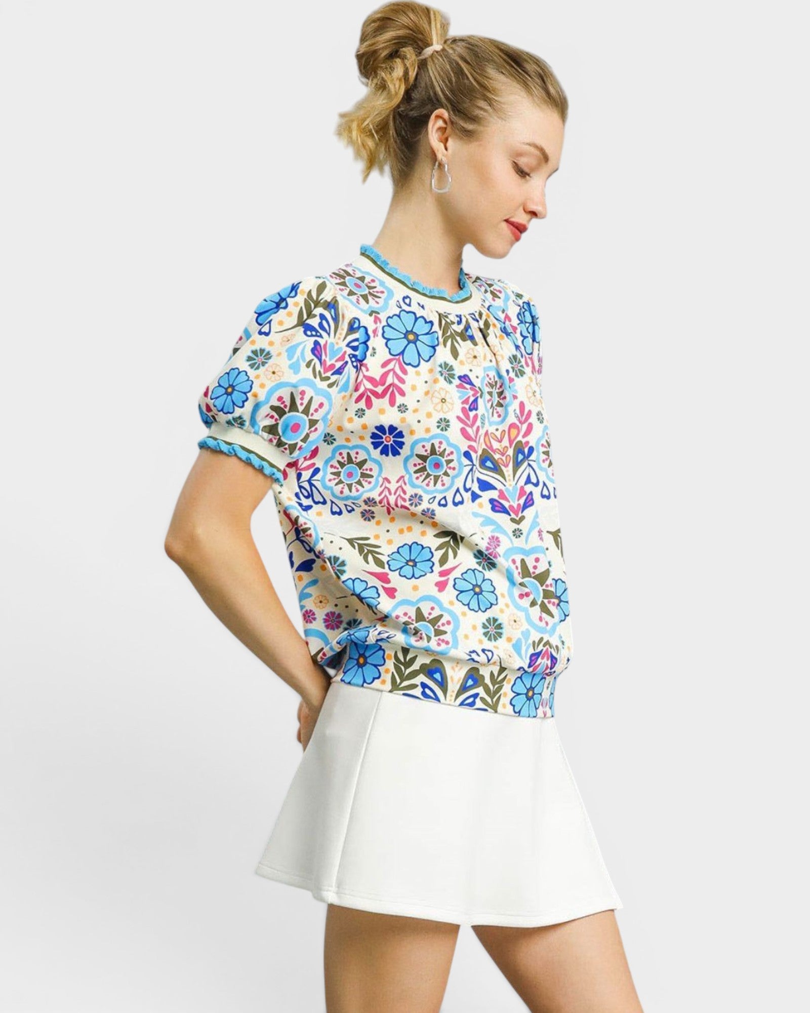 Woman wearing a colorful floral-patterned top and white skirt on a light gray background