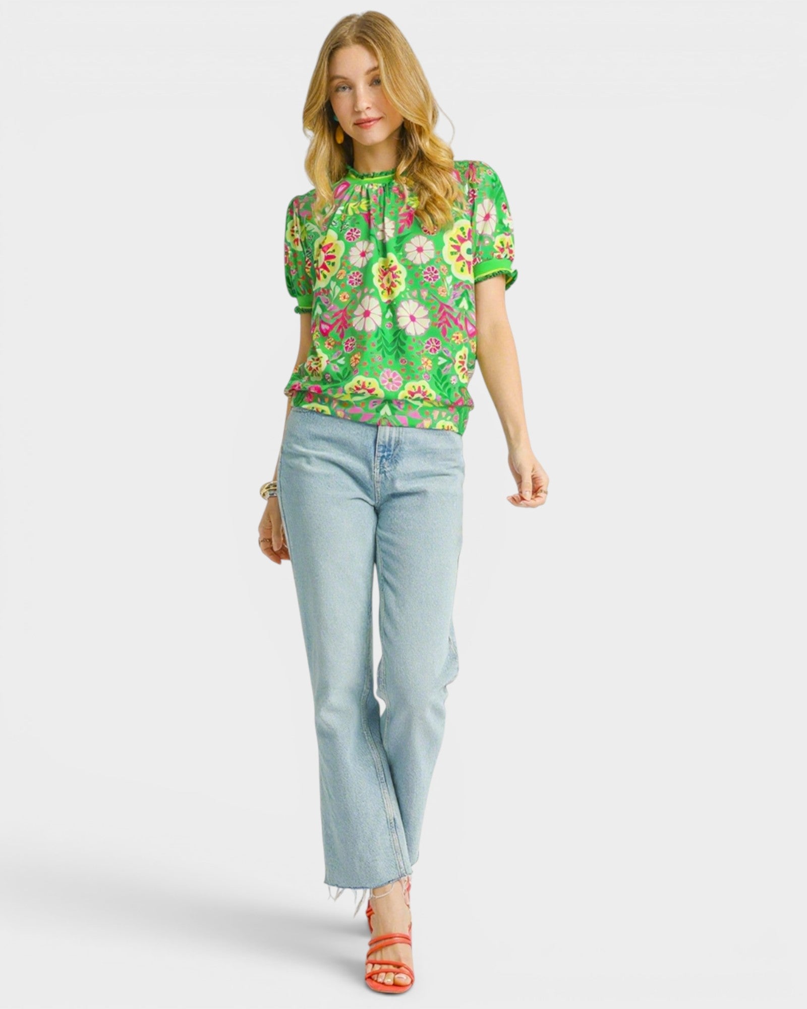 Woman wearing a floral green top and light blue jeans on a white background