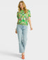 Woman wearing a floral green top and light blue jeans on a white background