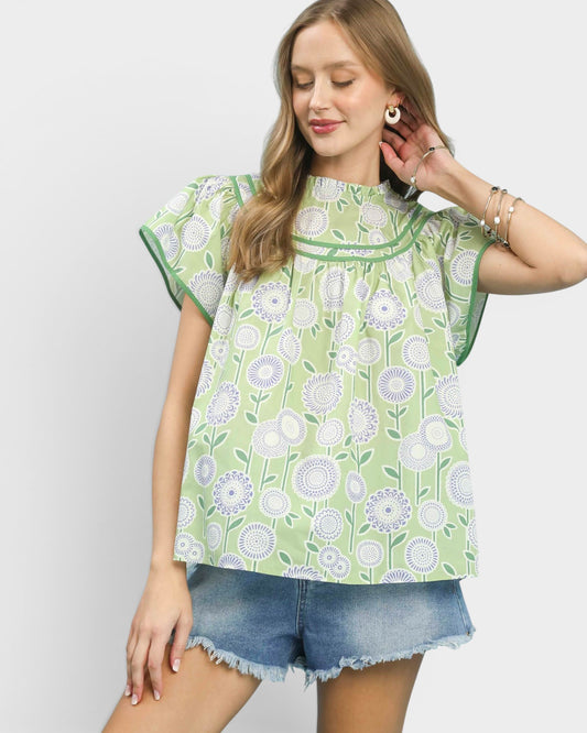 Woman wearing a green floral patterned top and denim shorts on a white background