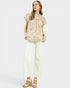 Woman wearing a floral top and white pants on a light gray background