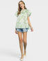 Woman wearing a green floral blouse and denim shorts on a white background