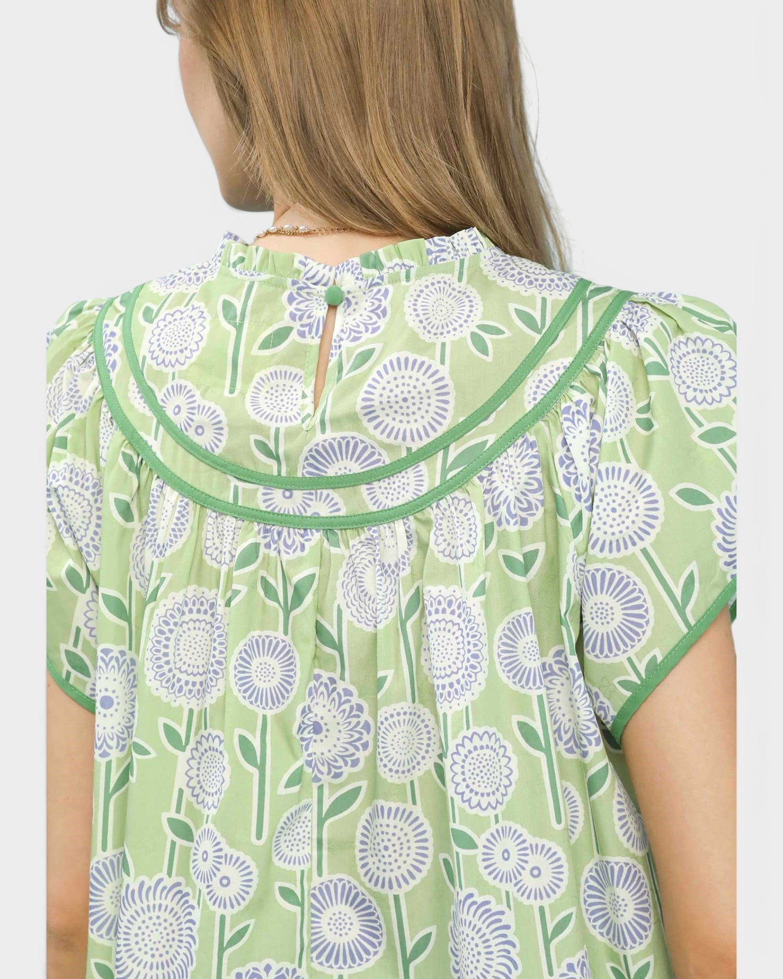 Green floral patterned top worn by a person on a white background
