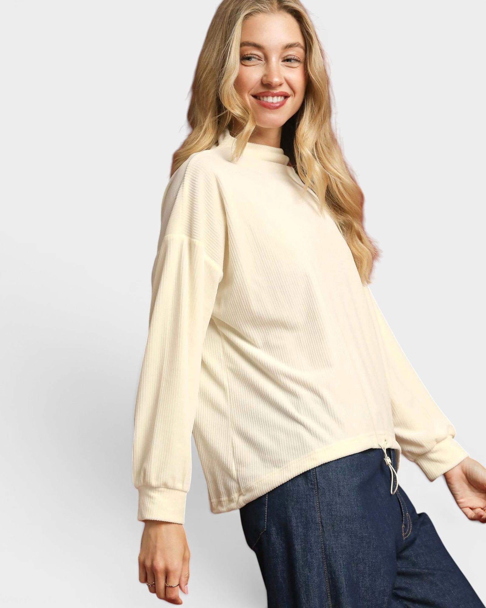Woman wearing a beige sweater and blue jeans on a white background