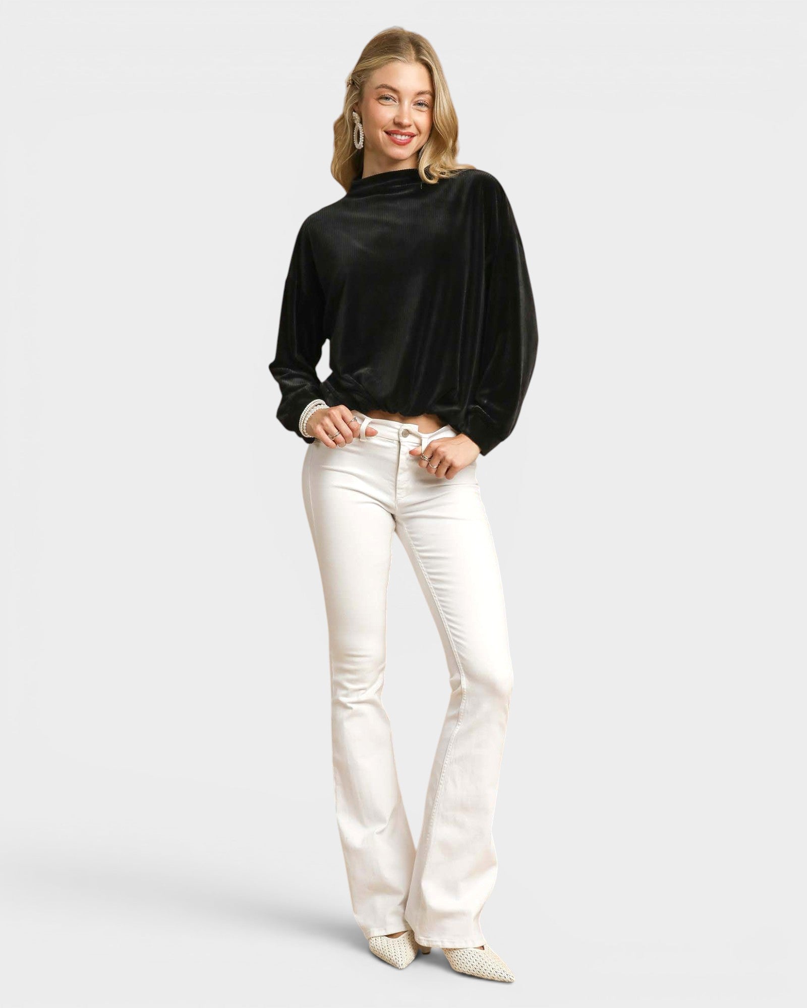 Woman wearing a black top and white pants on a light gray background