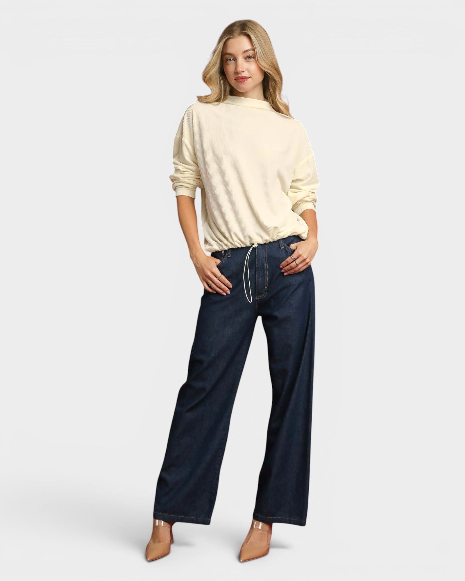Woman wearing a beige sweater and dark blue jeans on a white background