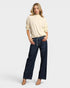 Woman wearing a beige sweater and dark blue jeans on a white background