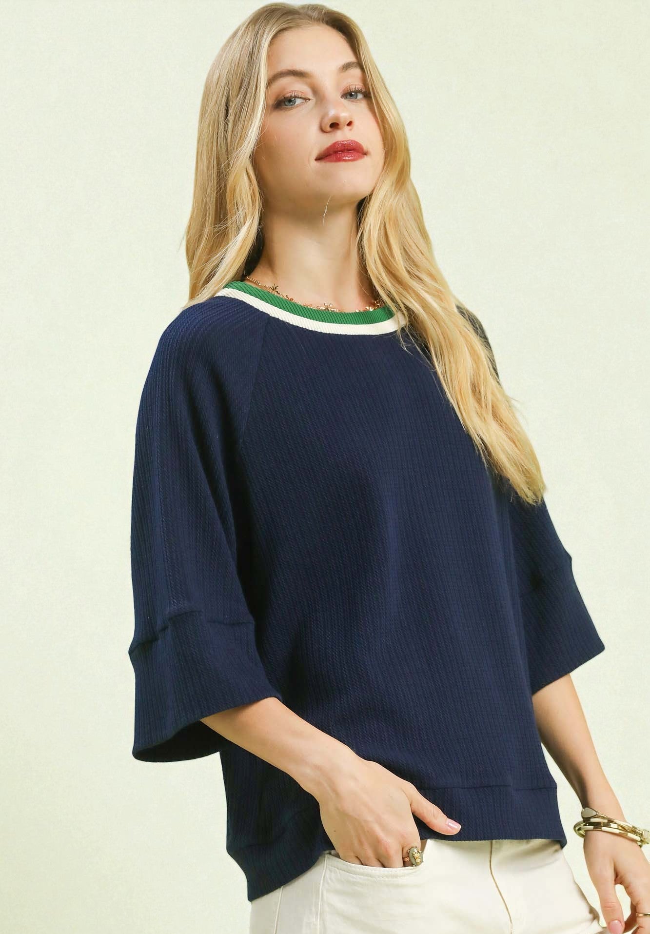 Woman wearing a navy sweater with a green and white trim on a beige background