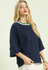 Woman wearing a navy sweater with a green and white trim on a beige background