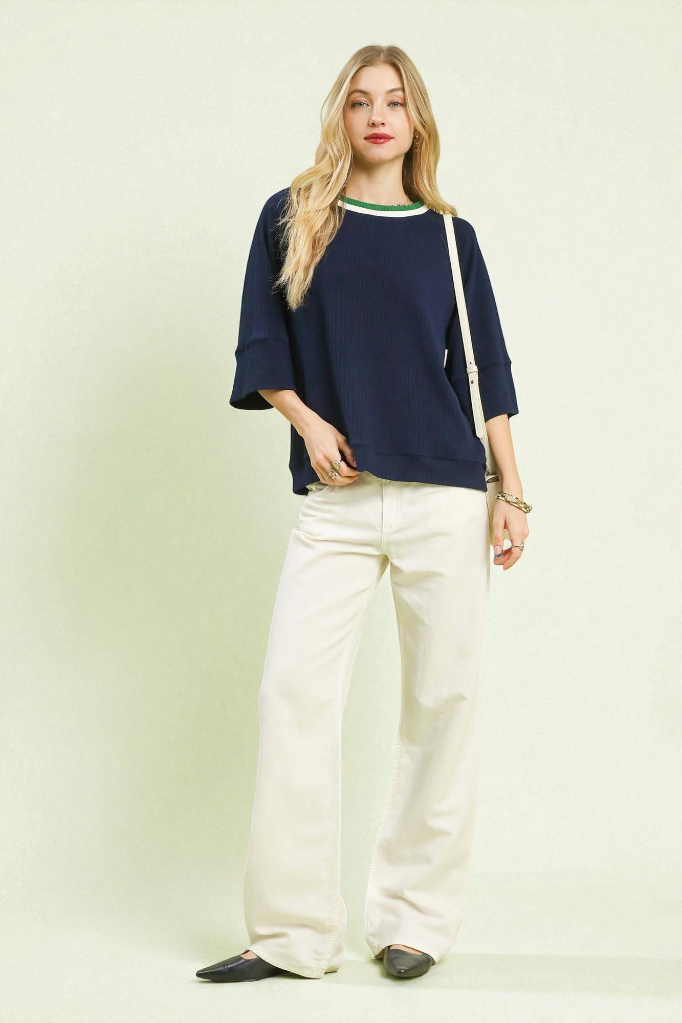 Woman wearing a navy blue top and white pants on a light green background