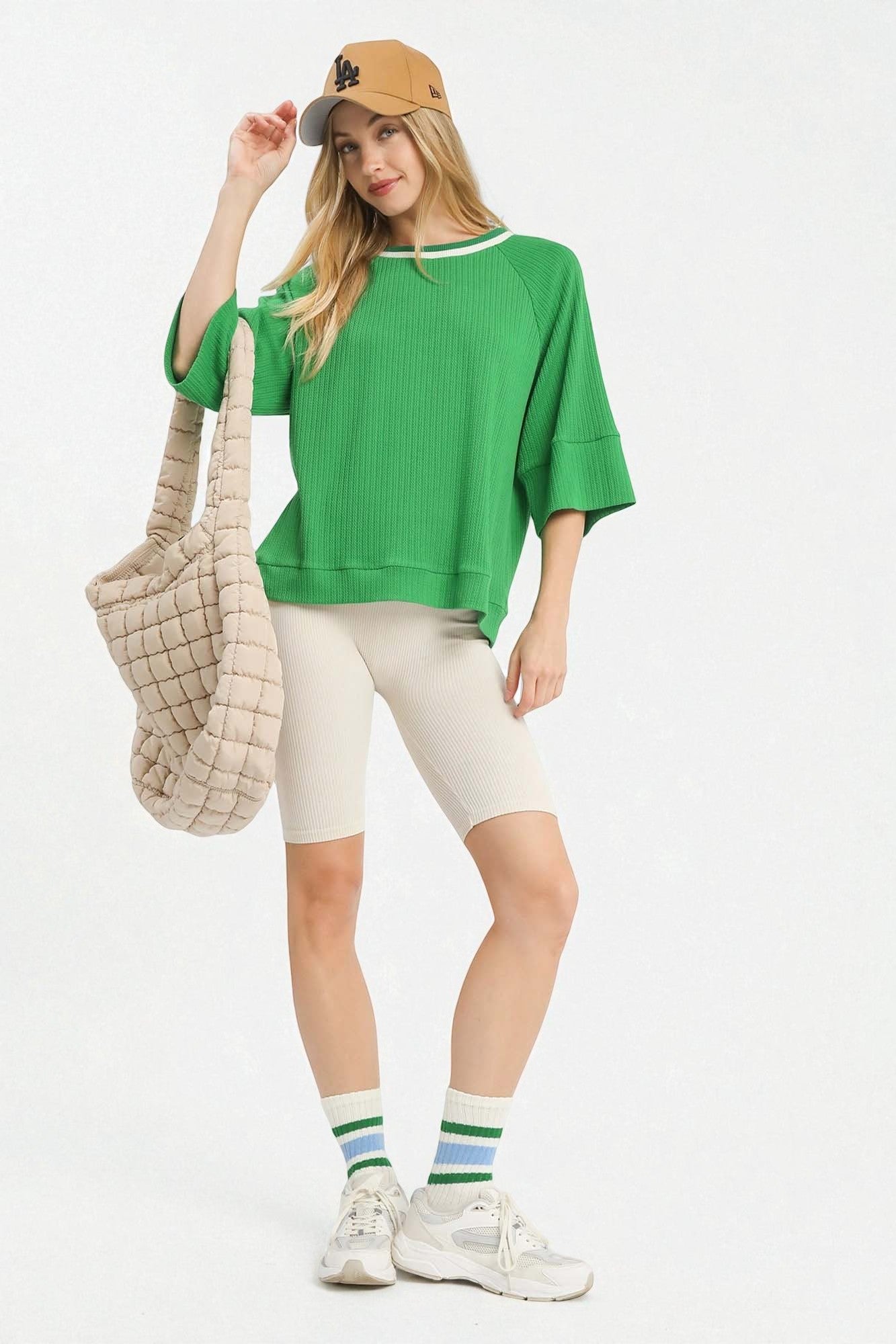 Woman wearing a green sweater, beige capri pants, and white sneakers on a white background