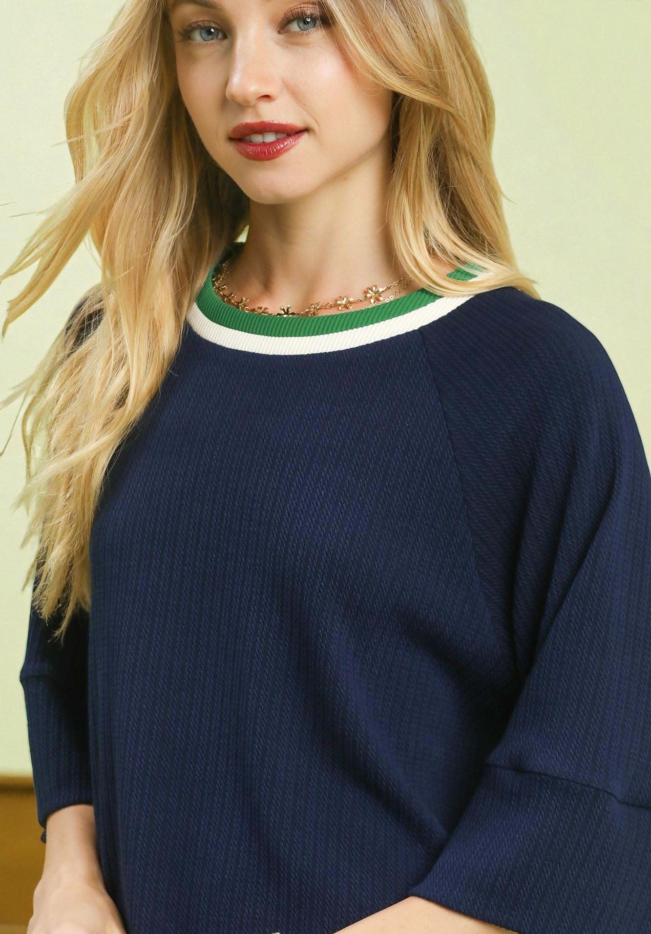 Woman wearing a navy sweater with green and white trim against a light background