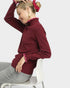 Woman wearing a burgundy sweater with pink trim sitting on a white chair against a light gray background