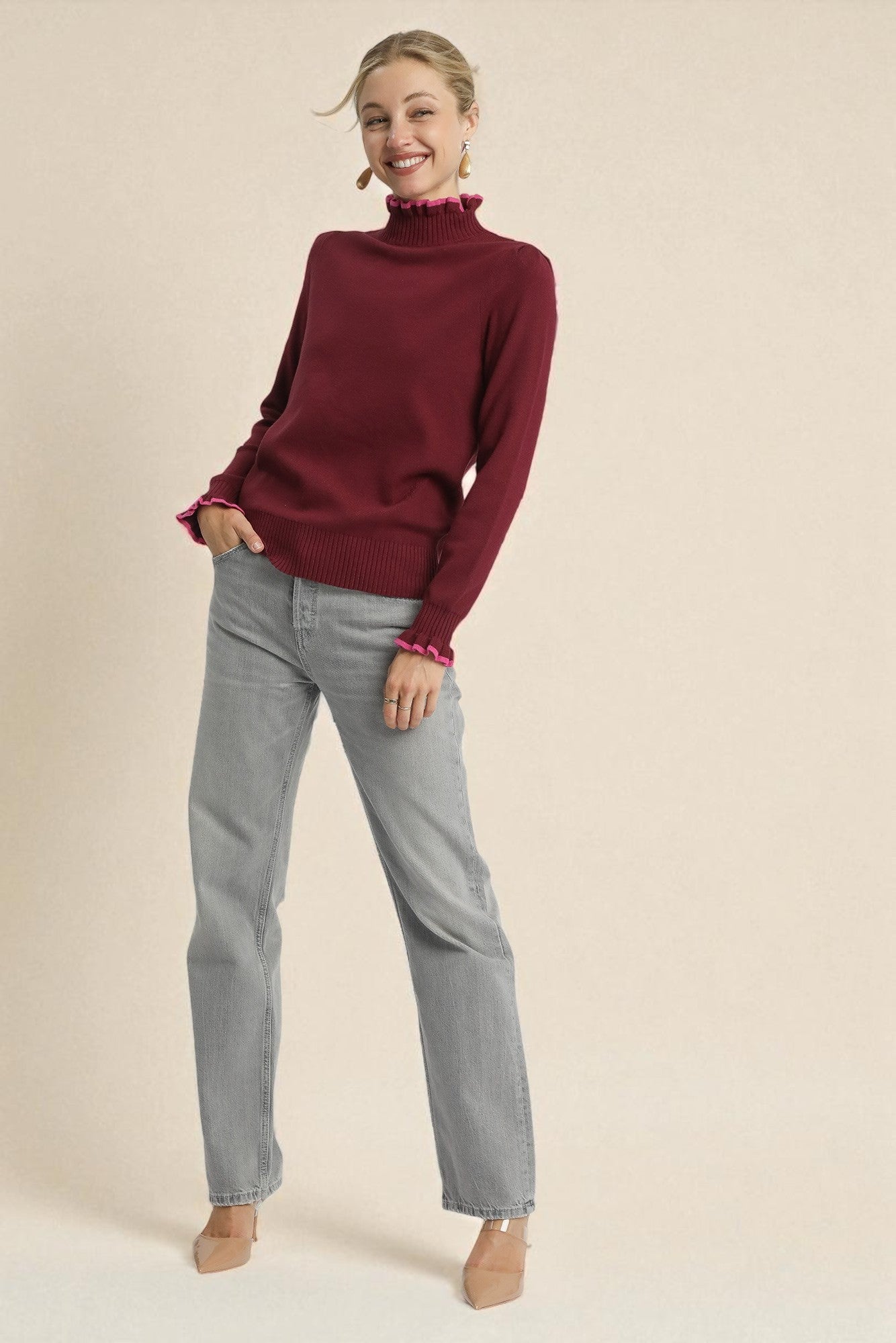 Woman wearing a burgundy sweater and gray jeans on a beige background