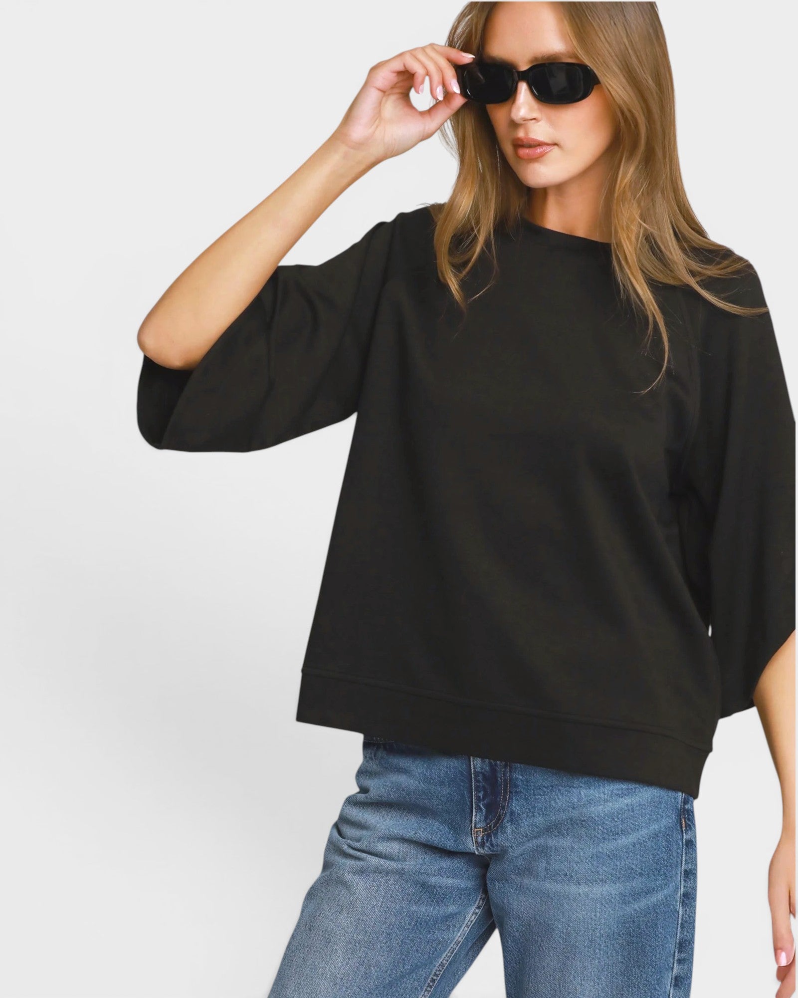 Woman wearing a black oversized sweater and blue jeans against a white background