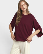 Woman wearing a burgundy sweater and white pants on a plain background