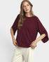 Woman wearing a burgundy sweater and white pants on a plain background