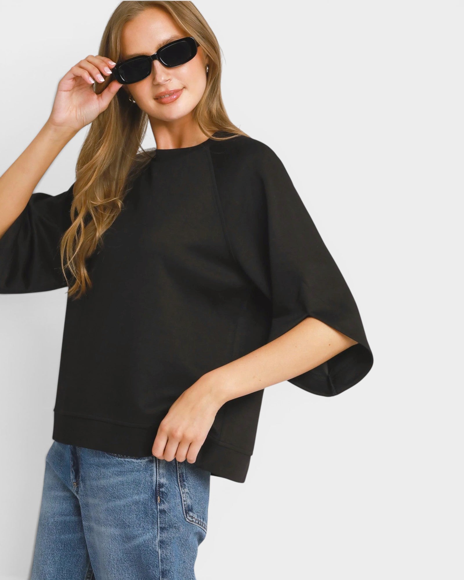Woman wearing a black oversized sweater and blue jeans against a white background