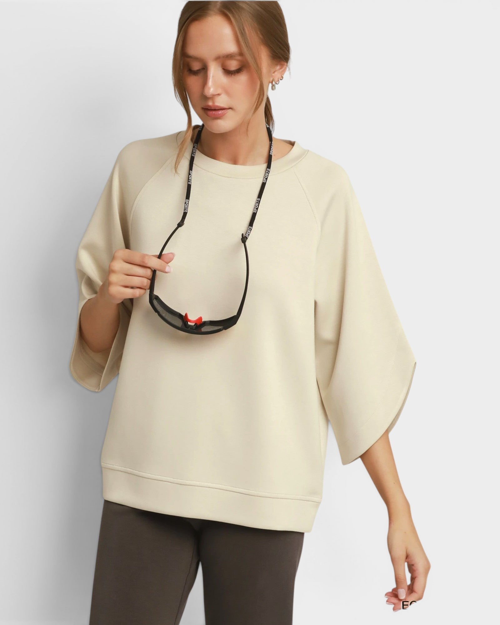 Woman wearing a beige sweater holding a black necklace with a red pendant on a light gray background