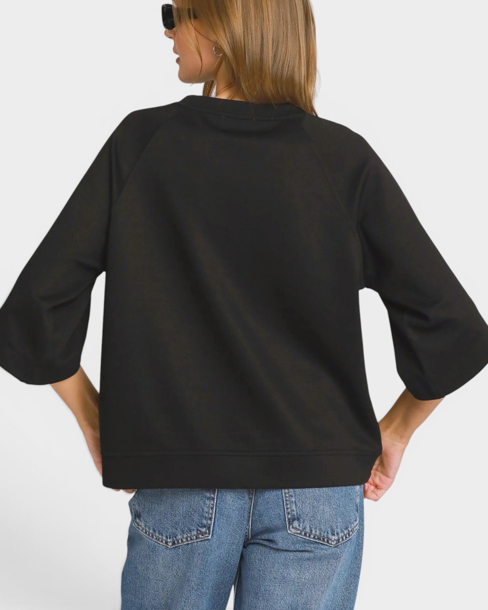 Person wearing a black oversized sweater and blue jeans on a white background