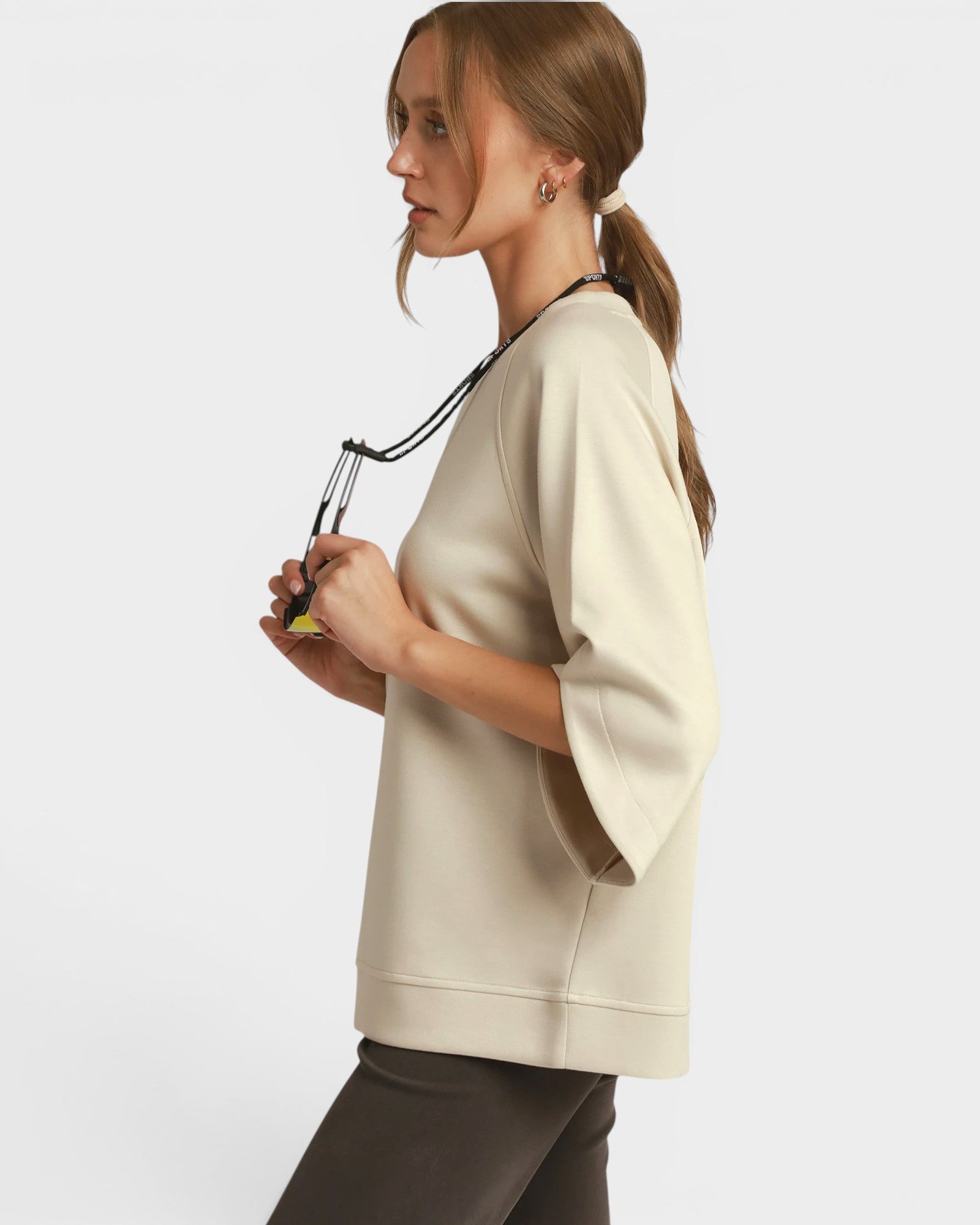 Woman wearing a beige sweater holding sunglasses on a white background