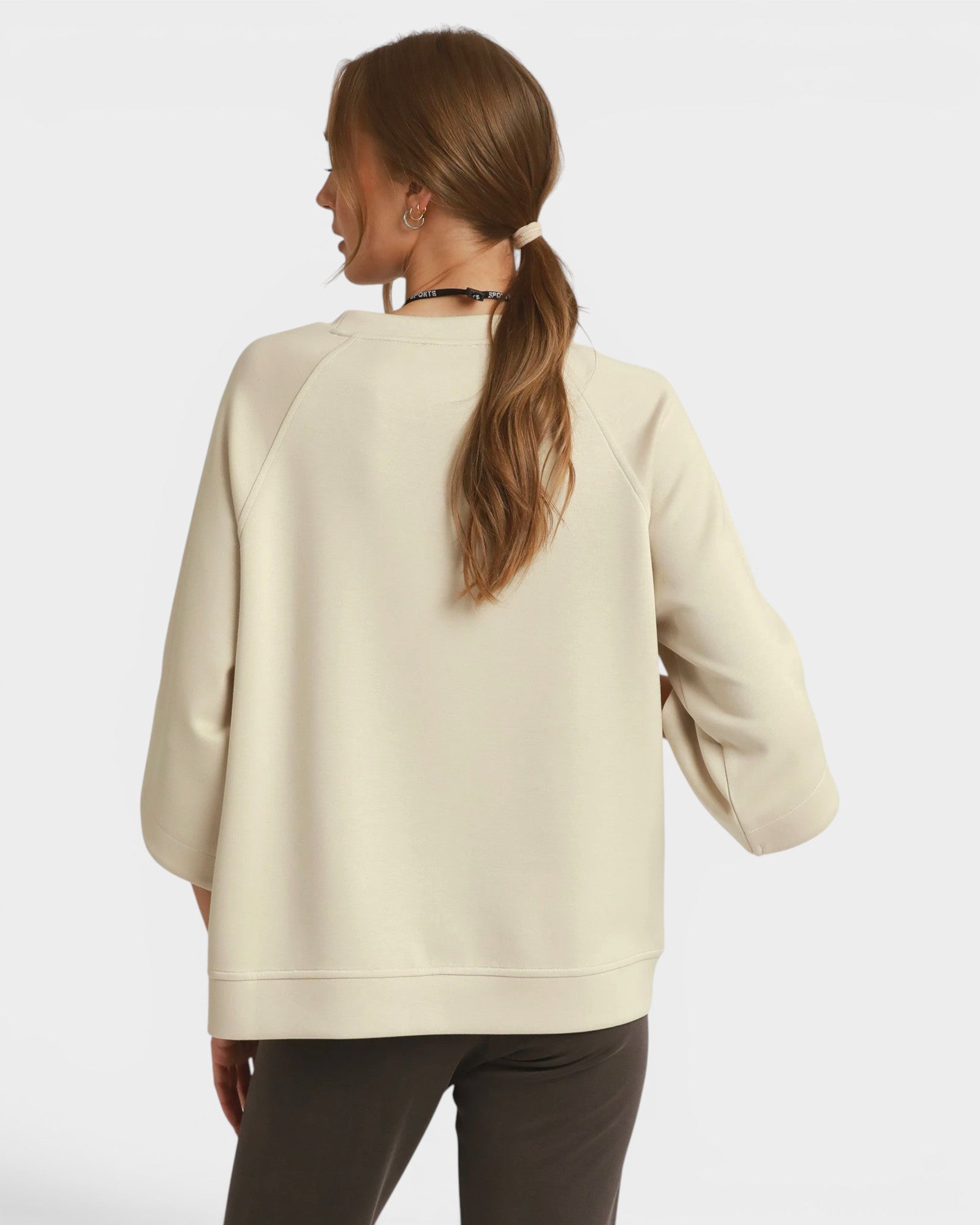 Woman wearing a beige oversized sweater with a plain background