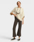 Woman wearing a beige top and dark pants on a white background