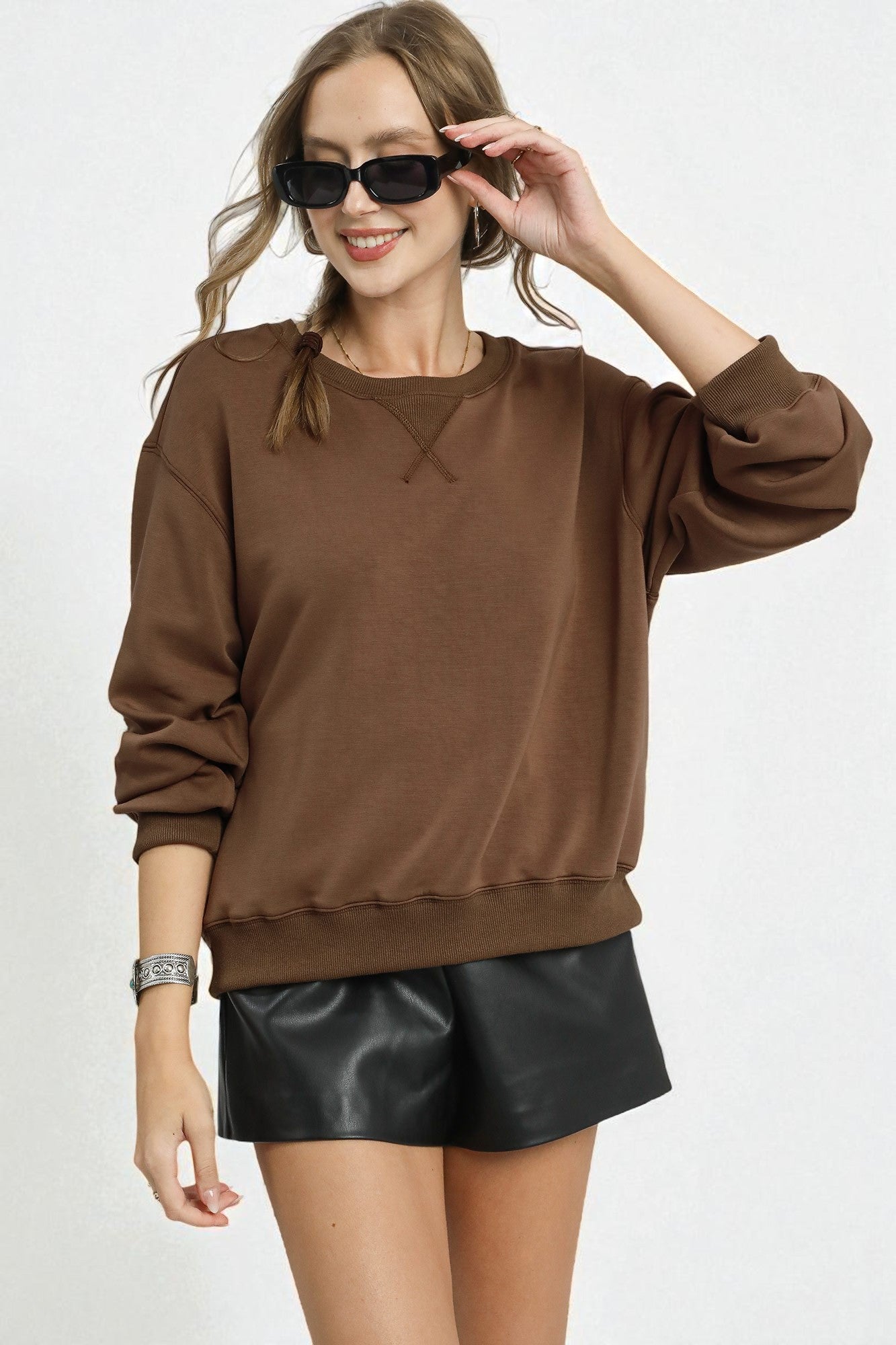 Woman wearing a brown sweatshirt and black leather shorts on a white background