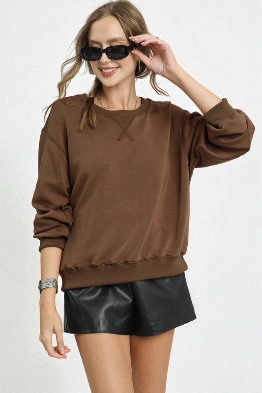 Woman wearing a brown sweatshirt and black leather shorts on a white background