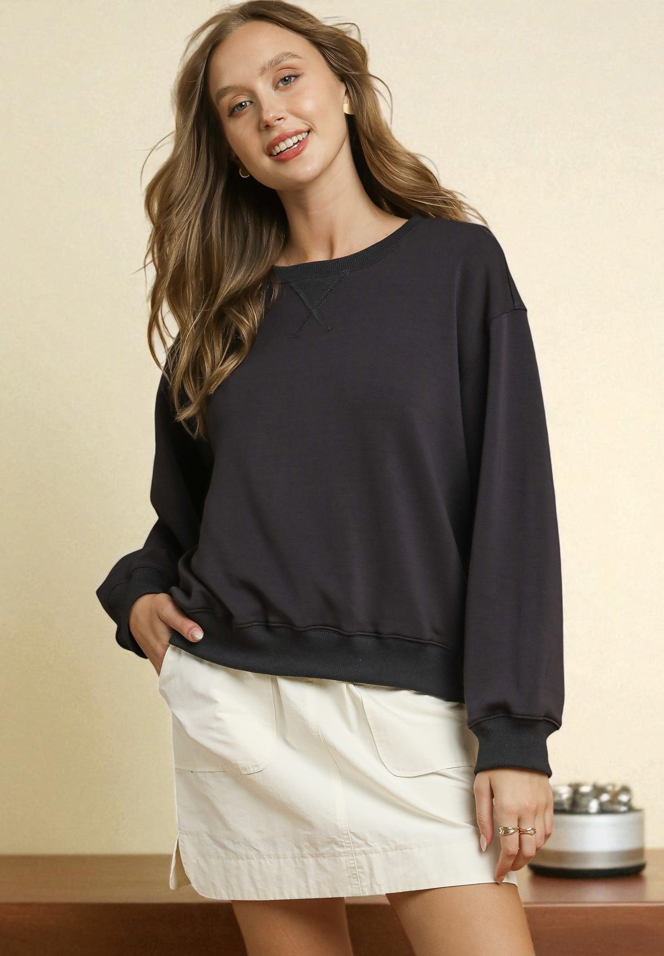 Woman wearing a black sweater and white skirt against a beige background