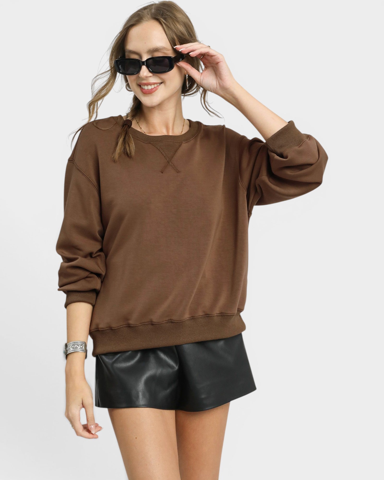 Woman wearing a brown sweatshirt and black leather shorts on a white background