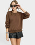 Woman wearing a brown sweatshirt and black leather shorts on a white background