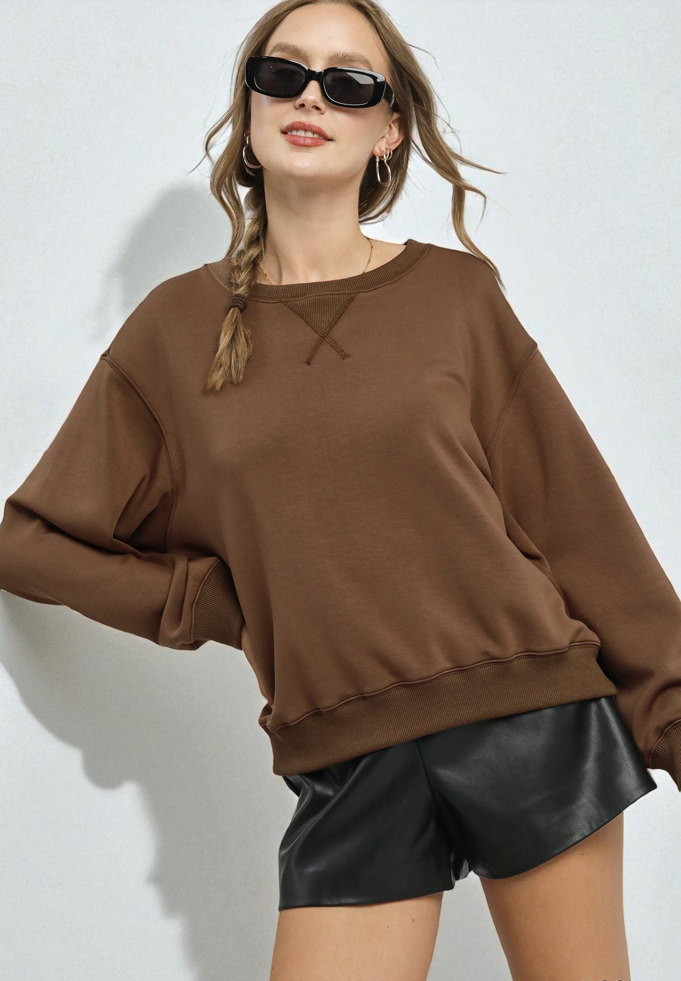 Woman wearing a brown oversized sweatshirt and black leather shorts on a white background