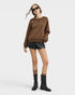 Woman wearing a brown sweatshirt, black leather shorts, and black boots on a white background