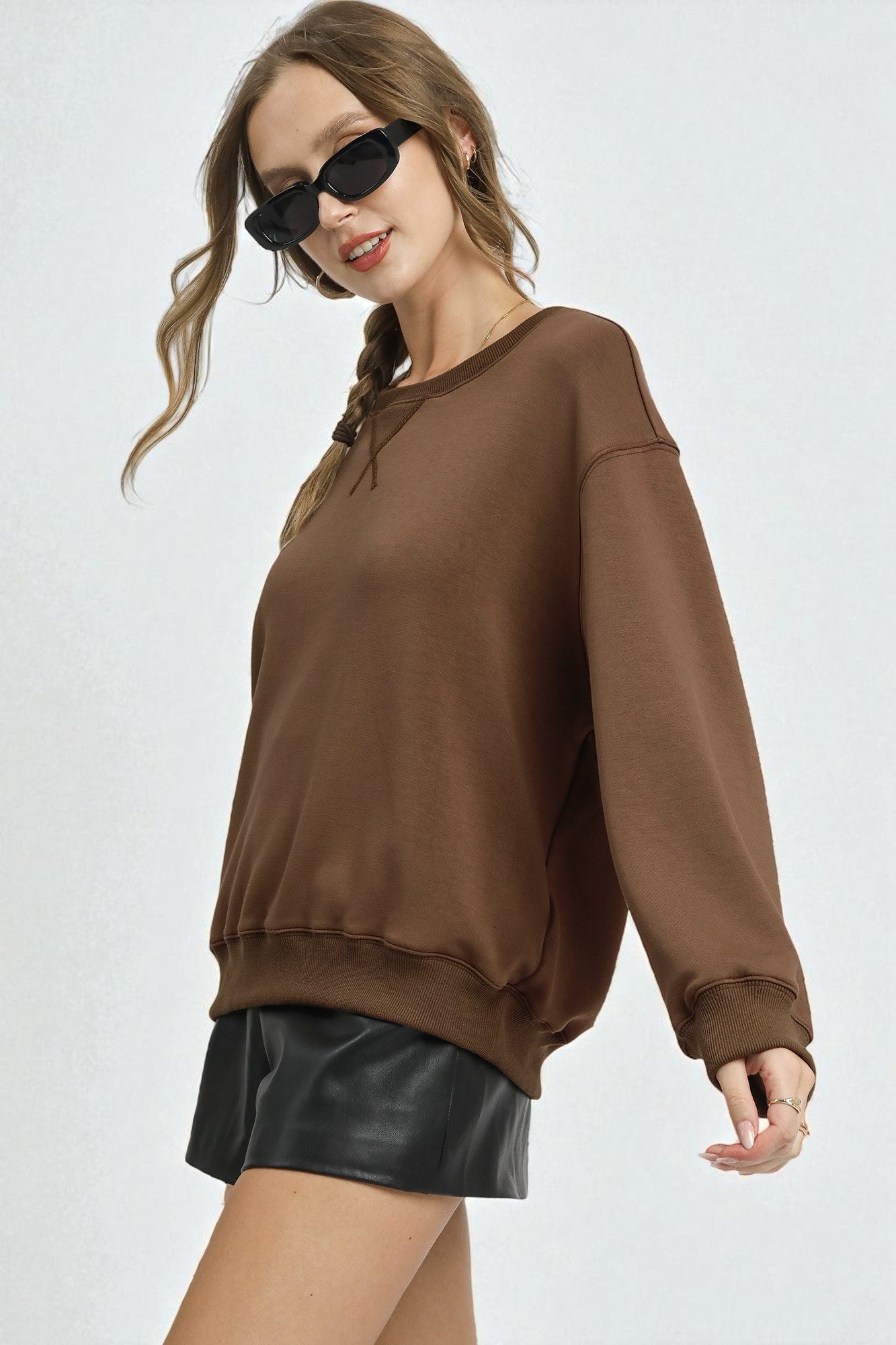 Woman wearing a brown sweatshirt and black leather shorts on a white background