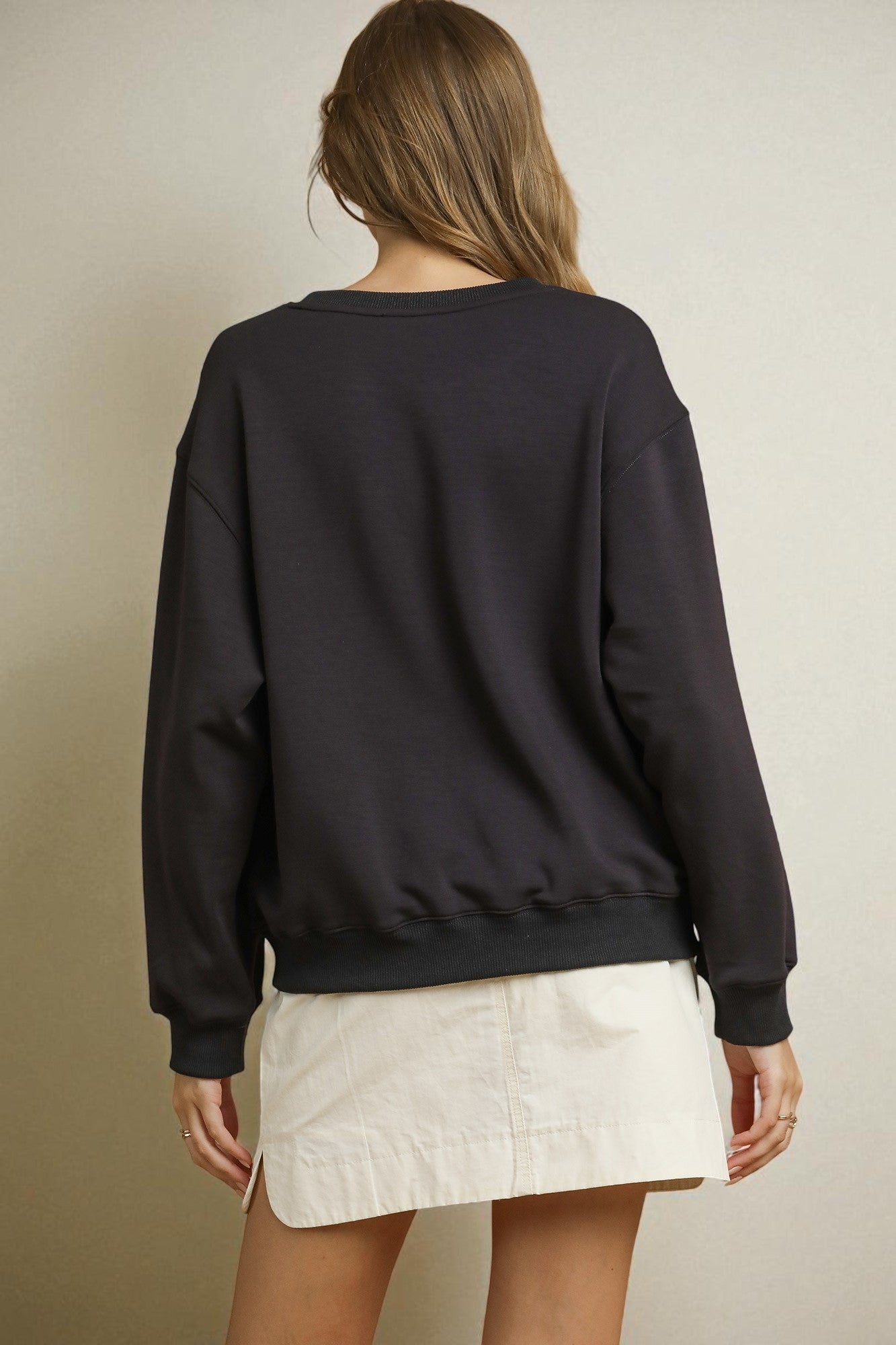 Person wearing a black sweatshirt and white skirt on a neutral background