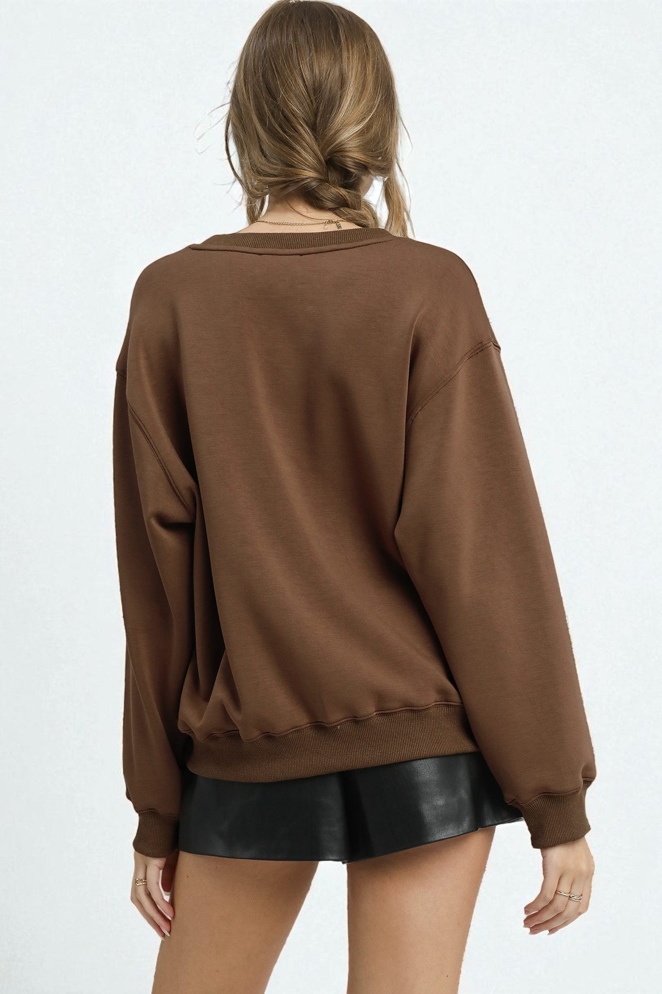 Person wearing a brown sweatshirt and black leather shorts on a white background