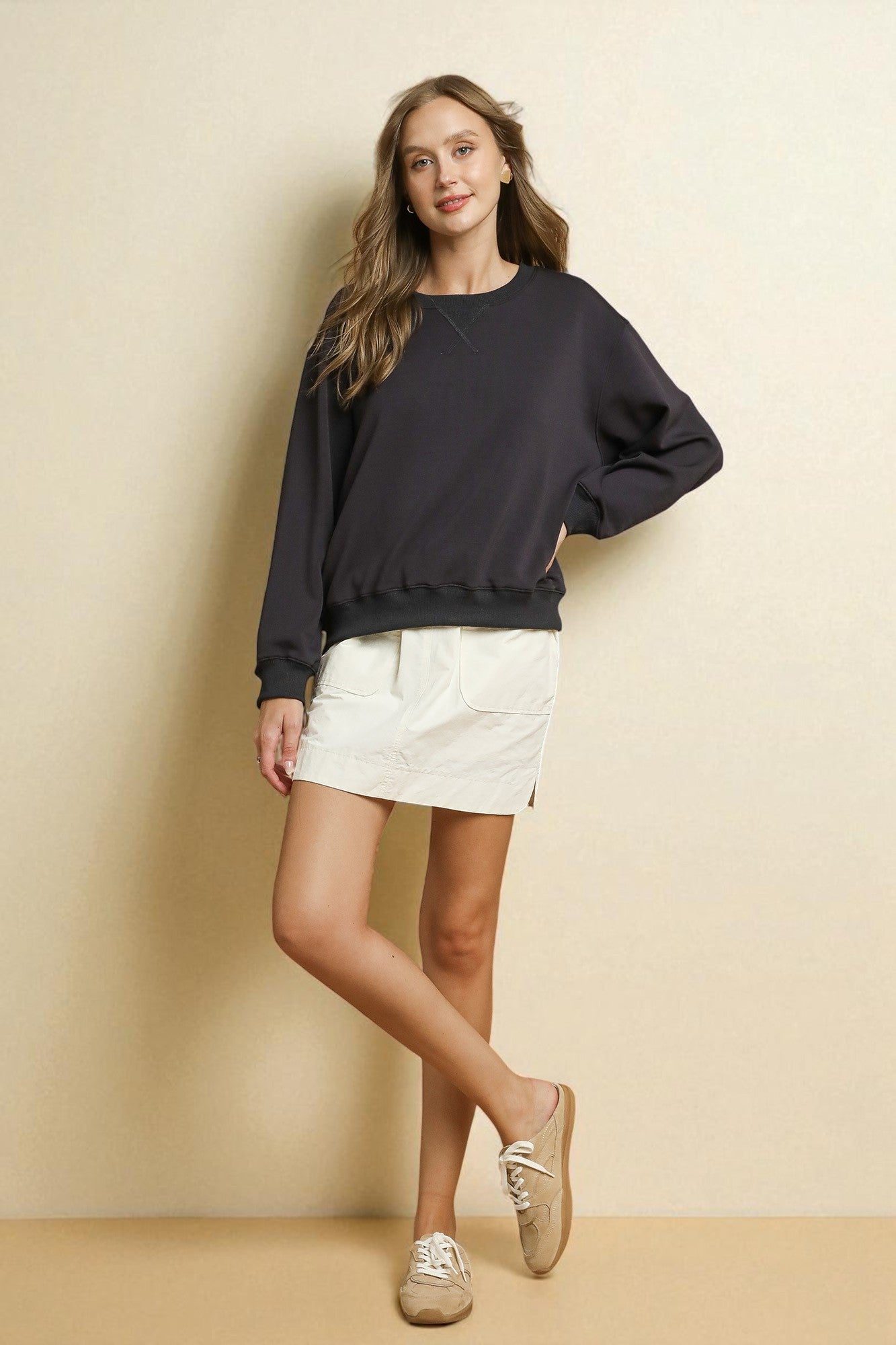 Woman wearing a black sweater and white shorts against a beige wall