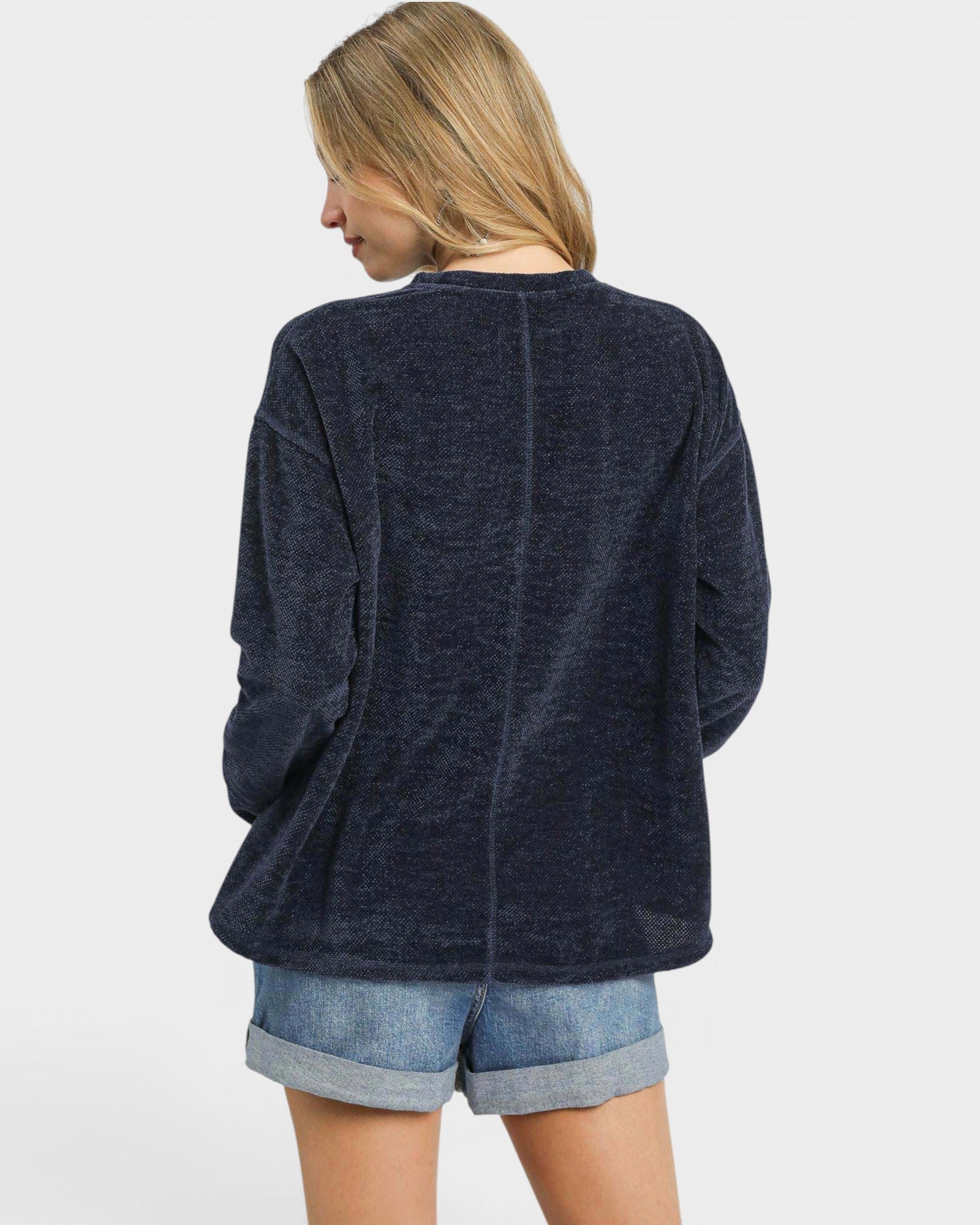 Woman wearing a navy blue cardigan over denim shorts on a light gray background