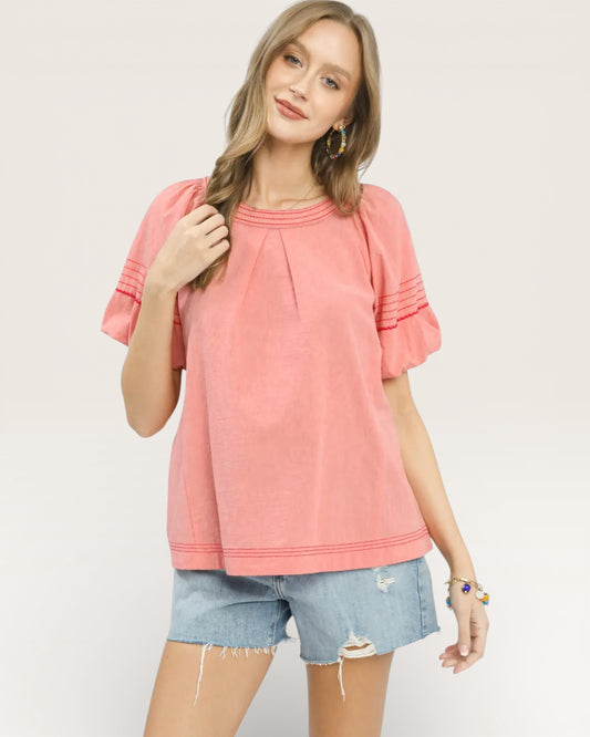 Woman wearing a pink top and denim shorts on a plain background