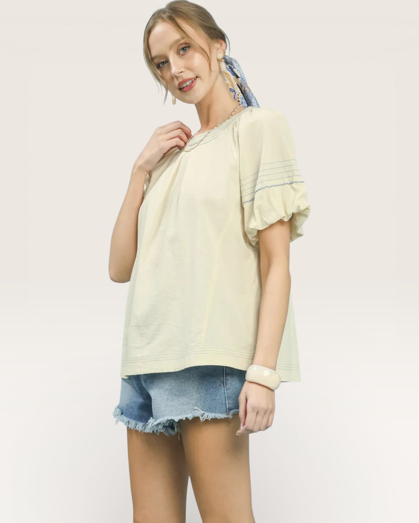 Woman wearing a light yellow blouse and denim shorts on a plain background