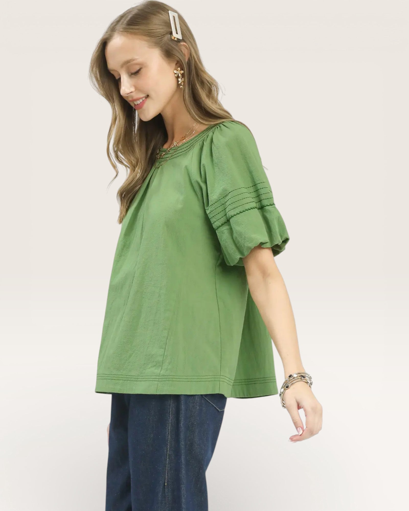 Woman wearing a green blouse with ruffled sleeves on a plain background